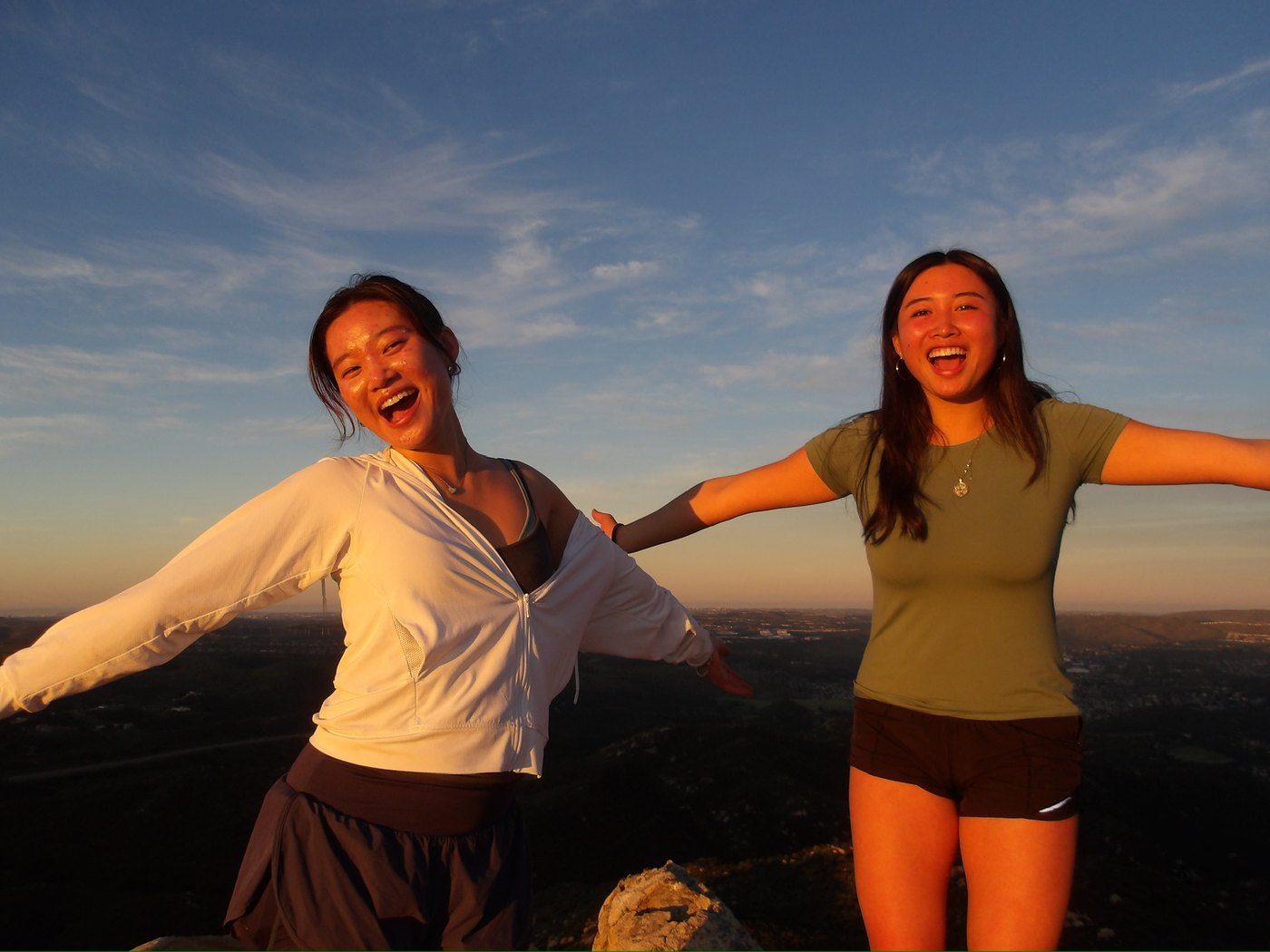 Two friends with arms open on a hill at golden hour